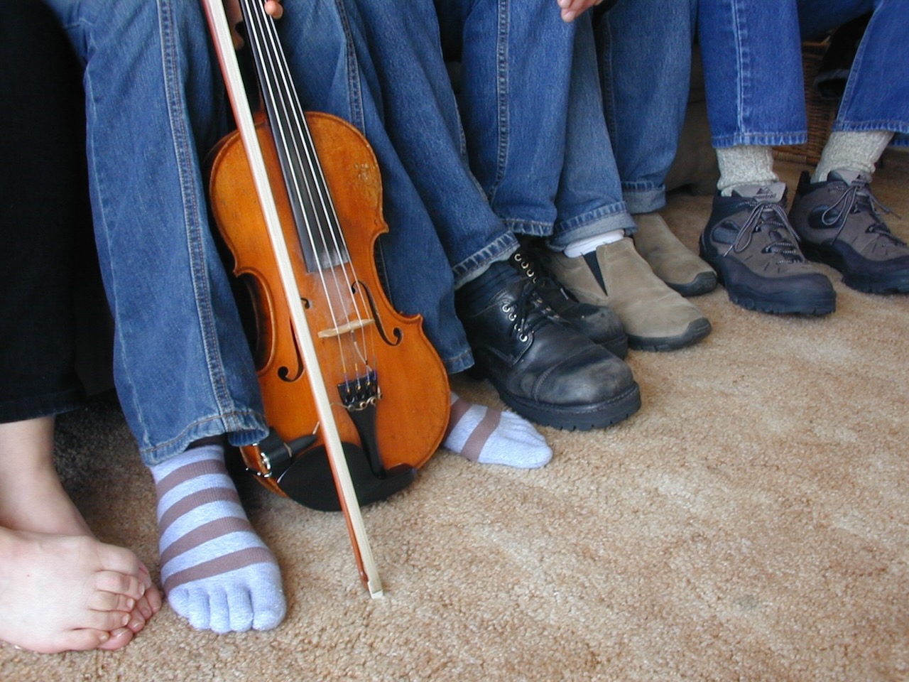 Five pairs of feet, one bare, one in striped toe socks, plus a fiddle